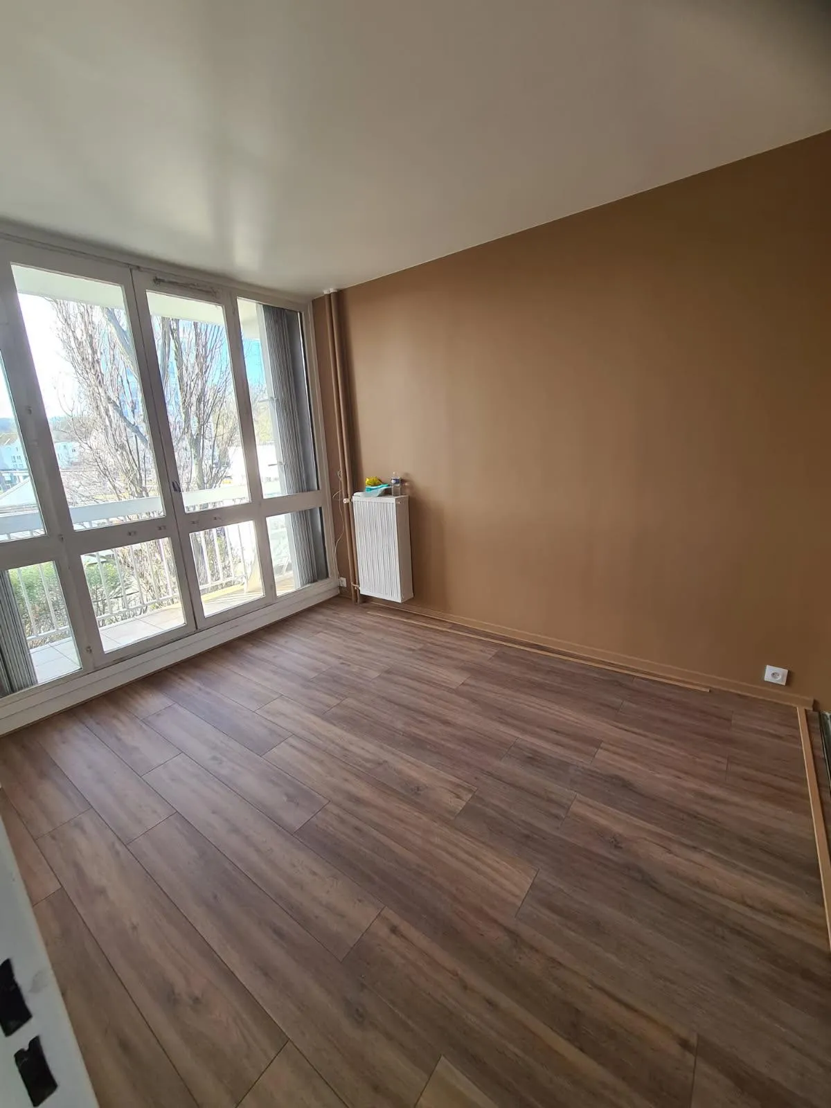 Pièce lumineuse avec un mur ocre, un plafond blanc et une grande fenêtre