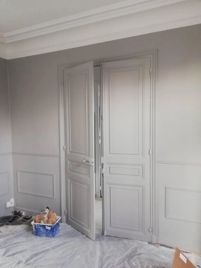 Double porte et murs gris moulurés, avec protections et matériel de chantier au sol