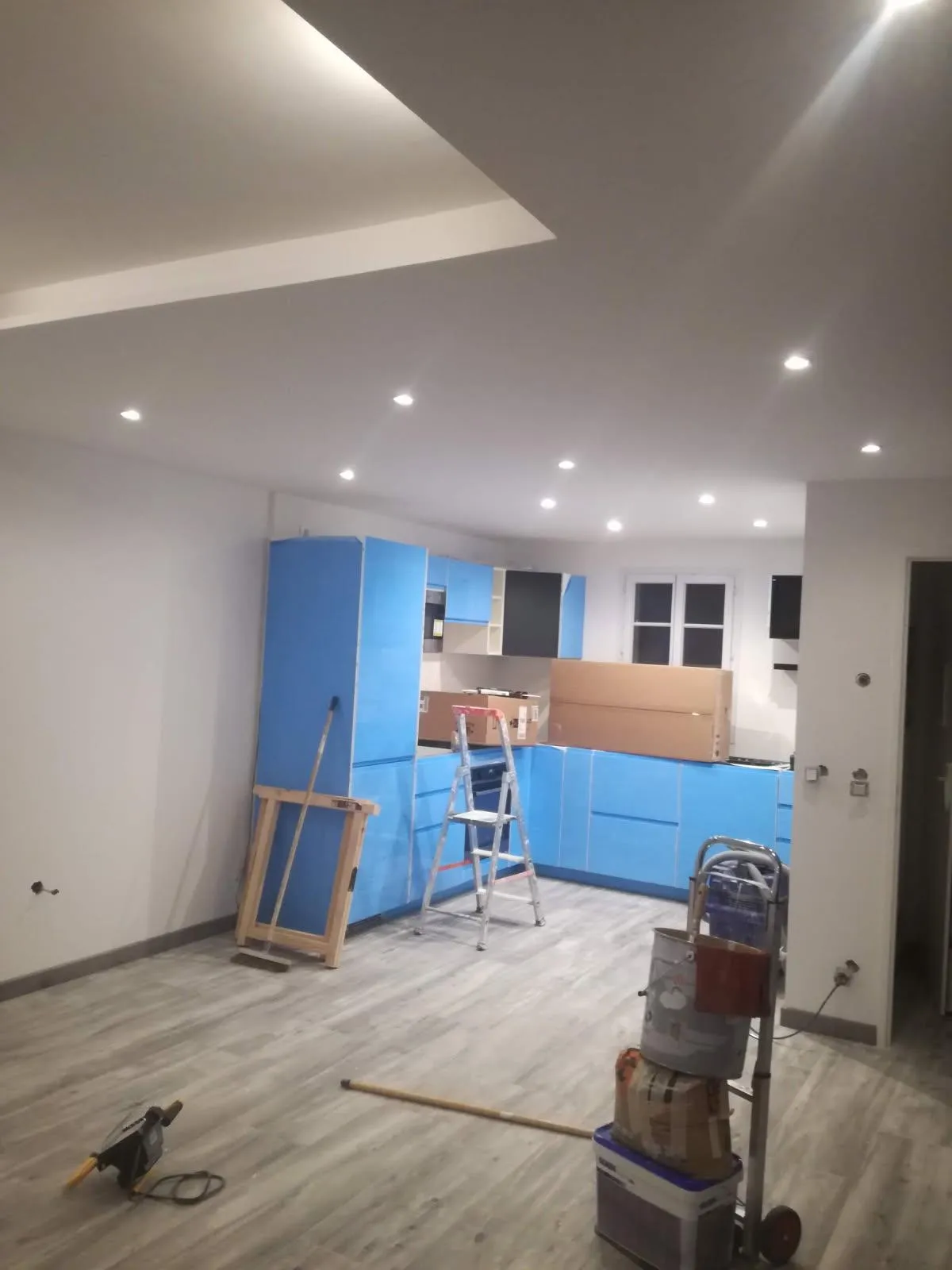 Pièce de vie en cours de rénovation, murs clairs, plafond avec spots et matériel de chantier